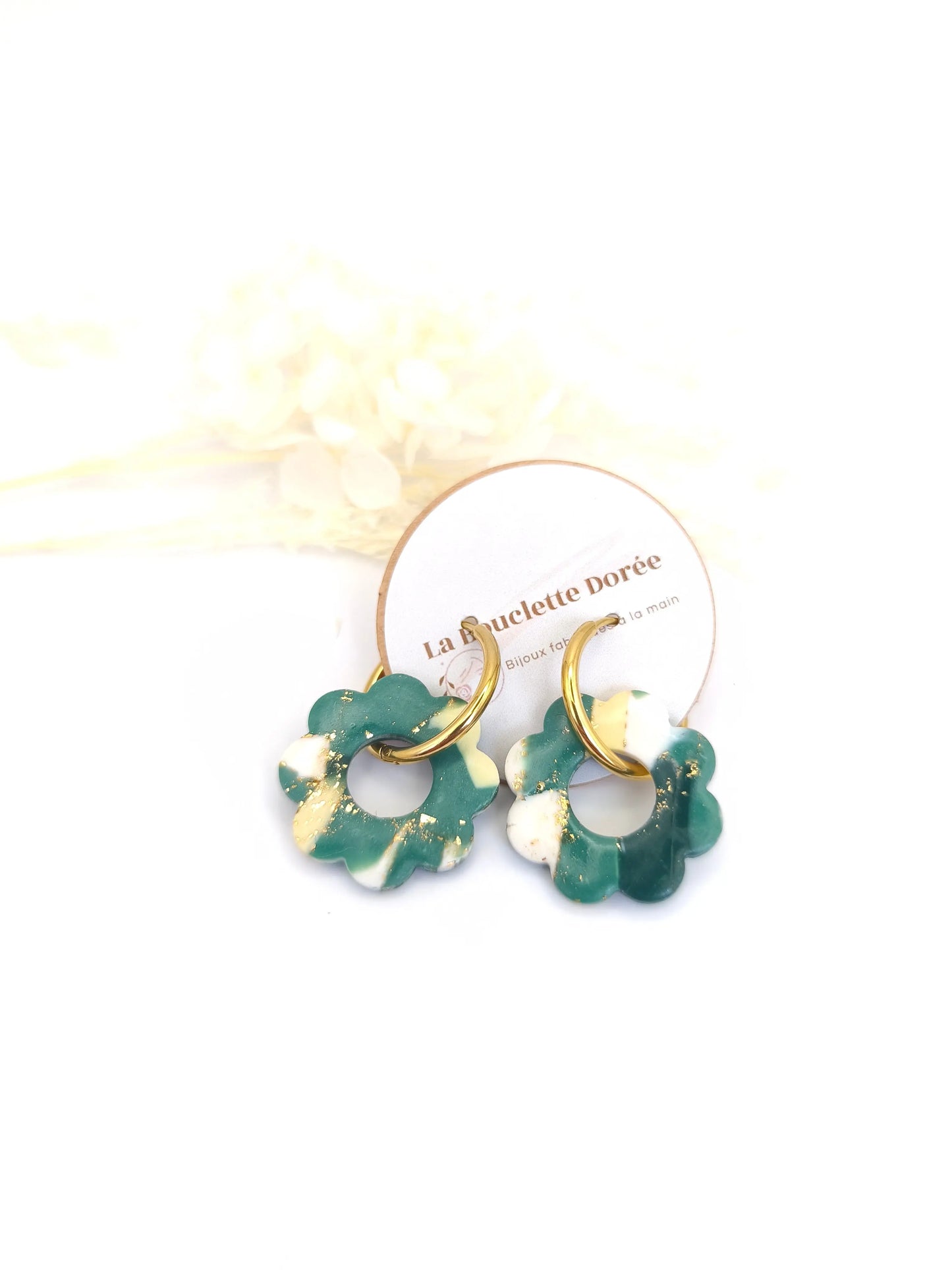 Boucles d’oreilles créoles en forme de fleur, dans les tons vert et jaune, posées sur fond neutre.